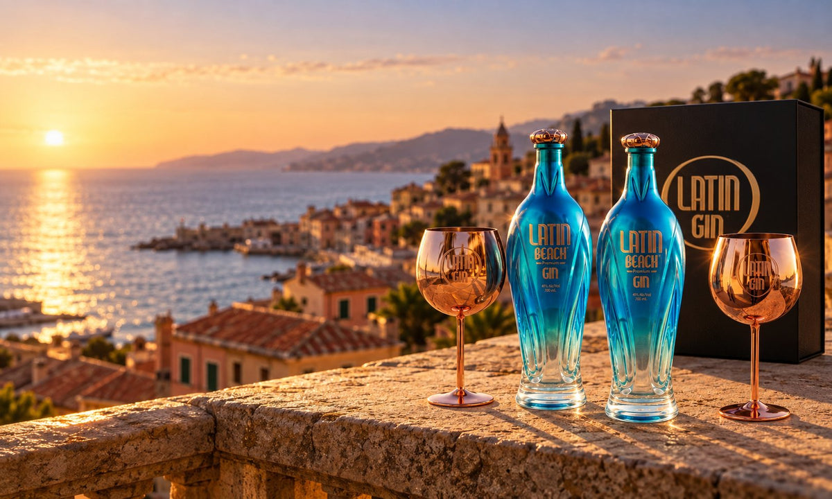 Two bottles of Latin Beach Gin, rose-gold copa glasses and the Latin Gin gift box on a terrace above an Italian coastal village at sunset